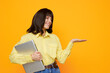 © SHOTPRIME STUDIO - A cheerful woman in a yellow shirt smiles while holding a laptop against a vibrant orange background, creating a friendly, approachable office or study scene.