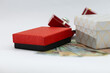 © Laurentiu Bratu - small red and white gift boxes with jewelry and scattered money on a white background, symbolizing expensive gifts, luxury, spending, and financial exchange