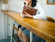 © Andika Nur - A girl's body in a gray skirt and white shirt sits in a cafe and holds an elegant tan leather handbag.