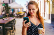 © Barillo Images - Woman with takeaway coffee checking her smartphone on city street.