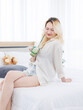 © Bangkok Click Studio - Asian beautiful attractive happy young woman blonde long hair wearing white shirt sitting on cozy bed natural light bedroom posing holding cold drink peaceful weekend morning at home lifestyle concept