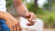 © Gethuk_Studio - Close-up of a hand holding a lit cigarette with smoke against a blurred green background.