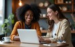 © fu - Dark skinned female graphic designer pointing with finger on laptop computer during collaboration with caucasian colleague on common project in coffee shop.Two multicultural friends discussing website