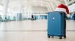 © Deamard - The concept of holiday travel is depicted by a piece of luggage wearing a Christmas hat against a background of blurred travelers and large windows.