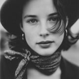 Klimatyczne, czarno-białe zbliżenie na twarz kobiety w kapeluszu i bandanie, z wyraźnym, przenikliwym spojrzeniem i młodzieńczym, naturalnym pięknem.