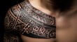 © Anjas - Close-up of a man's shoulder and chest adorned with a large, intricate black tribal tattoo design.