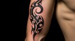 © Anjas - Close-up of a person's arm featuring a striking black tribal tattoo design against a dark background.