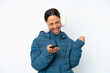 © luismolinero - Young hispanic woman wearing a winter earmuffs isolated on white background with phone in victory position