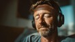 © Yuliia - Middle-aged Caucasian man with beard wearing headphones, eyes closed in peaceful expression while enjoying music in warm ambient lighting.