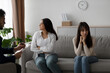 © Prostock-studio - Young Arab lesbian couple sits back to back in a therapist's office, seeking guidance to resolve their relationship conflict. Both women look thoughtful and concerned during the session.