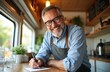 © Pete - Smiling mature man with glasses in apron writes on paper inside food truck. Owner manages small business, happy entrepreneur working outdoors.