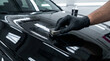 © Anastasiia Terenteva - Professional detailer hand in a black glove applying ceramic coating to a shiny black car hood