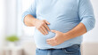 © Sunday Cat Studio - A man with a bloated belly holds his stomach in a calm indoor setting, reflecting health awareness.
