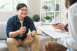 © KMPZZZ - Psychology, depression. smile asian young male, man patient mental sitting on couch, explained symptom with psychologist, psychiatrist while doctor woman taking notes at clinic. Encouraging, therapy.