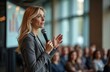© Pete - Blonde businesswoman speaks into microphone at business conference. Addresses large audience, actively presenting, engaging. Corporate data shows on screen. Pro manager talks at seminar, sharing