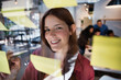 © Xavier Lorenzo - Smiling young woman writing notes on glass board during creative meeting. Focused professional contributing ideas in a modern collaborative workspace. Creativity and teamwork concept.