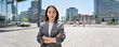 © insta_photos - Young confident smiling Asian business woman standing on busy street, portrait. Proud successful female entrepreneur wearing suit posing with arms crossed looking at camera in big city outdoors