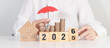 © Jo Panuwat D - 2025 end year to Happy New Year 2026 with red umbrella over money stack. Insurance, real estate, Home loan, tax, investment, mortgage, financial, savings, protection and safety