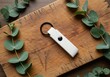 © Habiba - White leather keychain with black button detail resting on a rustic wooden cutting board surrounded by fresh eucalyptus leaves for a natural aesthetic