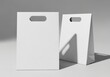 © MDJamir - Two blank white paper shopping bags with cut-out handles sit on a light surface casting shadows.