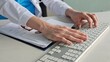 © Nadzeya - Hands of a medical professional typing on a keyboard while reviewing documents and files