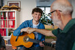 © Halfpoint - Group of elderly people singing together with young volunteer playing guitar.