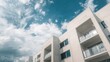 © vxnaghiyev - A section of a white residential building featuring balconies under a blue cloudy sky, showcasing modern architectural design