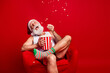 © deagreez - Santa relaxes in a red chair eating popcorn during Christmas eve in a cozy home setting with festive mood