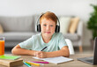 © Prostock-studio - Cheerful redhead boy participates in an online lesson from his home. He uses a laptop and headphones while taking notes and preparing for his educational project, enjoying the learning experience.