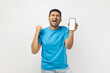 © khosrork - Joyful positive man showing blank white screen of cell phone, clenches fist, rejoicing his success.