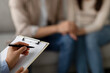 © Prostock-studio - In a therapy session, a marital counselor takes notes on a clipboard while meeting with an arab couple. The couple engages in conversation about their relationship challenges and goals.