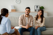 © Prostock-studio - A happy middle eastern couple sits on a couch at a counselor's office. They engage with the counselor, smiling as they listen attentively to advice about family relationships and communication.