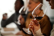 © Seventyfour - Diverse group of middle aged adults sampling red wine, holding glasses close to faces and examining color and aroma, participating in wine tasting session at table