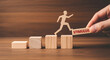 © Pixel Studio - Wooden figure climbing blocks with a hand placing a 'stimulus' block symbolizing growth and economic recovery set against a warm wooden background ideal for financial concepts