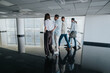 © qunica.com - Several coworkers move along a glossy, modern office corridor, carrying bags and files as they walk together, reflecting teamwork, planning, and everyday business life.