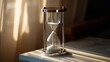 © Plaifah - Elegant hourglass filled with white sand on a sleek table, sunlight streaming through curtains in a calm indoor setting, time concept imagery