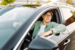 © maxbelchenko - A young man wearing glasses sits behind the wheel of a car on a sunny day. The smiling driver enjoys the view from the window. Conceptual concepts: transportation, leisure.