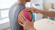 © David Zarzosa - Sports therapy session applying kinesiology tape to athlete’s shoulder in physiotherapy clinic.