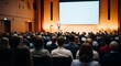 © tarik - Rear view of people in the audience at a business event conference hall, speaker presenting on stage, emphasizing audience engagement, corporate learning, professional communication and leadership.