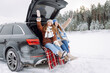 © maxbelchenko - Happy female friends sit on a blanket in the trunk of a car, having fun on a winter day. Two young women enjoy a road trip in a snowy forest. Concepts of friendship, relaxation, and adventure.