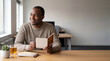 © Nikhil - A thoughtful professional finds a spark of inspiration, pen in hand, as he holds a card, with a cup of tea by his side and gazing out the window. Christmas gift card, middle aged blackman