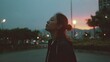 © mila103 - A woman stands in a city park at sunset gazing upward with a serene expression. The vibrant colors of the sky illuminate her surroundings creating a peaceful atmosphere.