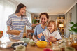 © Stockphotodirectors - A family shares a joyful breakfast at home, with a mother serving food while a father happily interacts with their young child. The cozy atmosphere has natural light streaming in.