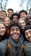 © Анастасія Шестопал - A diverse group of young friends is happily smiling and posing for a cheerful outdoor group selfie together.