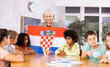 © JackF - High school teacher, conducting a lesson in the classroom, tells the pupils the history of Croatia and holds the national flag .of the country in her hands
