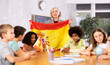 © JackF - Woman teacher tells pupils about Spain in a history lesson and holds the national flag of the country