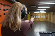 © Dmitri - Rear view of blonde woman practicing with golden handgun at indoor shooting range wearing ear protection