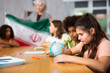 © JackF - Female high school teacher, conducting a lesson in the classroom, tells pupils the history of Iran and holds the national .flag of the country