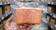 © Bakha - Vacuum sealed fresh salmon fillet held in hand at warehouse storage aisle, showcasing quality packaged seafood product ready for distribution and modern food supply chain logistics