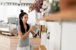 © NAMPIX - A young Asian woman with her hair in a bun wipes a surface with a cloth, standing in her shop